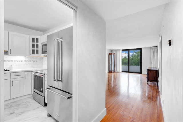 600 Three Islands Blvd Unit 310, Hallandale Beach, FL 33009 - kitchen featuring stainless steel appliances, white cabinetry, decorative backsplash, glass insert cabinets, and light countertops