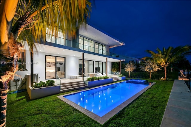 1410 S Biscayne Point Rd, Miami Beach, FL 33141 - back of house at night with an in-ground hot tub, stucco siding, a yard, and an outdoor pool