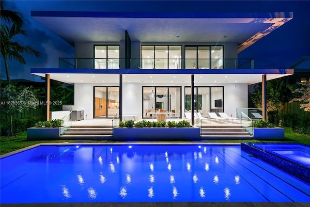 1410 S Biscayne Point Rd, Miami Beach, FL 33141 - back of house at night featuring a balcony, a patio, stucco siding, an outdoor pool, and an in-ground hot tub