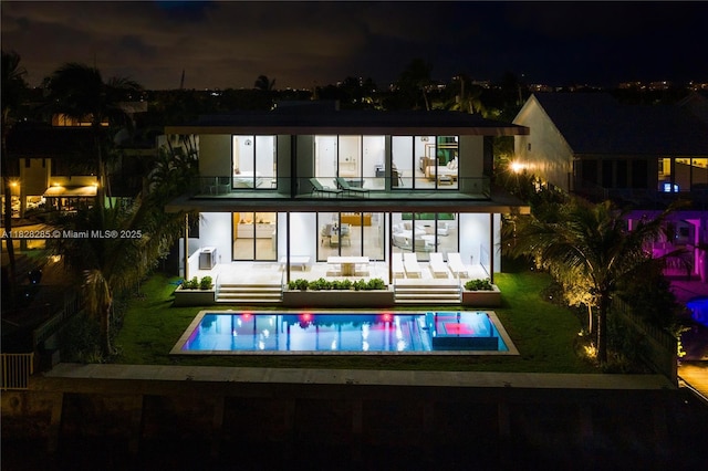 1410 S Biscayne Point Rd, Miami Beach, FL 33141 - back of house at twilight featuring a balcony, a lawn, and an outdoor pool