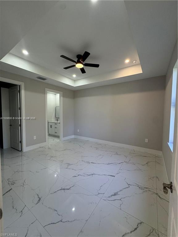 3003 18th St W, Lehigh Acres, FL 33976 - unfurnished bedroom featuring a tray ceiling, recessed lighting, ensuite bathroom, light marble finish flooring, and ceiling fan