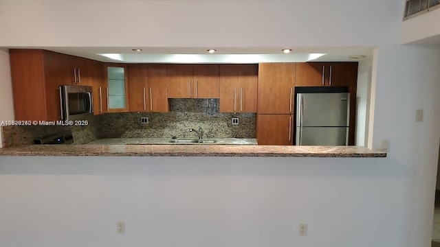 19380 Collins Ave Unit 808, Sunny Isles Beach, FL 33160 - kitchen featuring freestanding refrigerator, decorative backsplash, glass insert cabinets, light stone counters, and brown cabinets