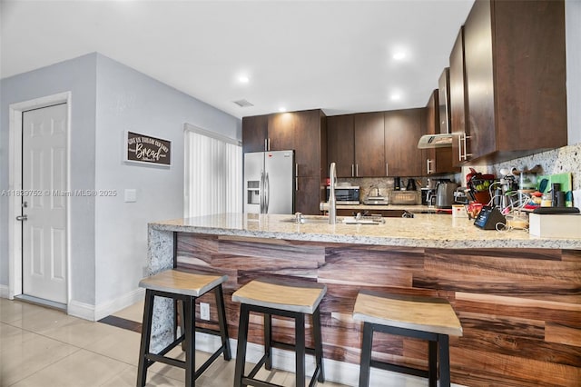 17625 NW 62nd Ct, Hialeah, FL 33015 - kitchen featuring stainless steel refrigerator with ice dispenser, a peninsula, dark brown cabinetry, decorative backsplash, and light stone countertops