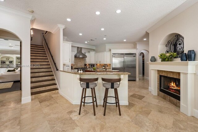 2211 Azalea Pl, Winter Park, FL 32789 - kitchen featuring stainless steel built in refrigerator, wall chimney exhaust hood, a peninsula, stone counters, and crown molding