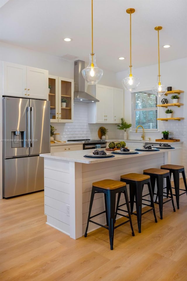 2607 Lafayette Ave, Winter Park, FL 32789 - kitchen featuring stainless steel fridge, wall chimney range hood, light wood finished floors, a kitchen breakfast bar, and tasteful backsplash
