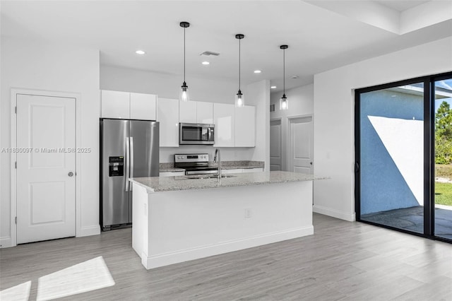 933 Gleason St, Lehigh Acres, FL 33974 - kitchen featuring appliances with stainless steel finishes, white cabinetry, light wood-type flooring, a kitchen island with sink, and light stone counters
