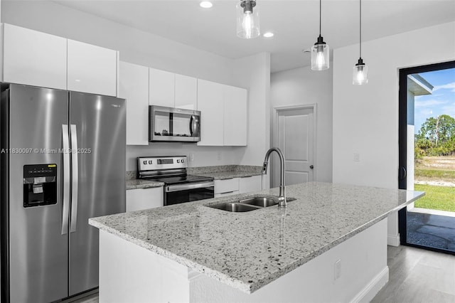 933 Gleason St, Lehigh Acres, FL 33974 - kitchen featuring appliances with stainless steel finishes, white cabinetry, light wood-style flooring, decorative light fixtures, and a center island with sink