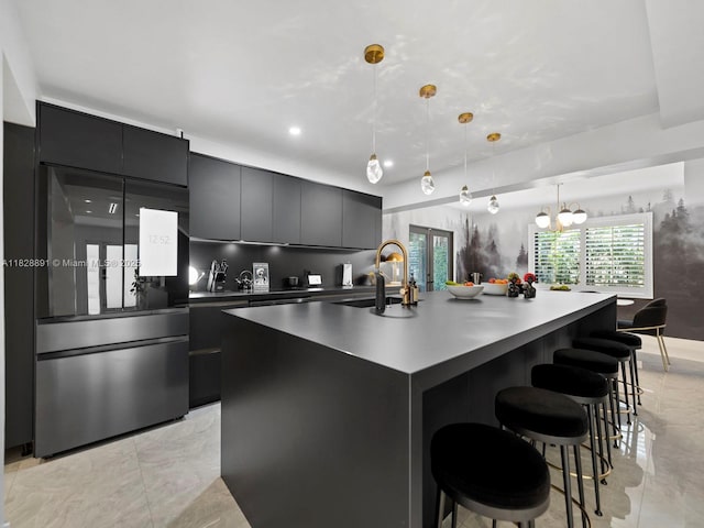 1117 Alberca St, Coral Gables, FL 33134 - kitchen with dark cabinetry, freestanding refrigerator, a center island with sink, modern cabinets, and decorative light fixtures