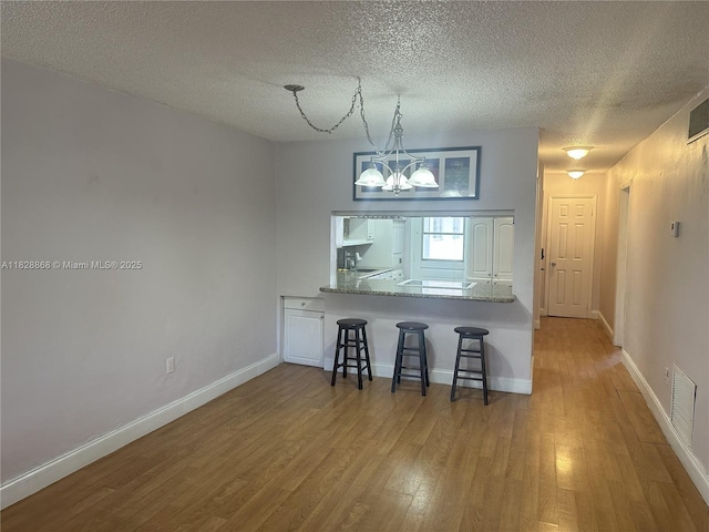 251 Galen Dr Unit 112E, Key Biscayne, FL 33149 - kitchen featuring wood finished floors, a breakfast bar, a chandelier, a textured ceiling, and pendant lighting