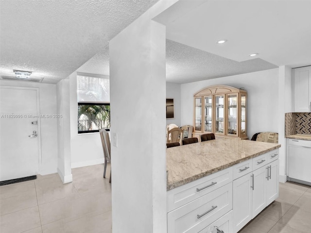 20401 NE 30th Ave Unit 310-8, Aventura, FL 33180 - kitchen featuring a textured ceiling, light tile patterned flooring, white cabinetry, backsplash, and light stone countertops