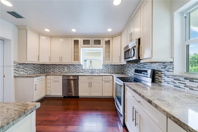 431 Gerona Ave, Coral Gables, FL 33146 - kitchen featuring appliances with stainless steel finishes, light stone counters, decorative backsplash, glass insert cabinets, and dark wood-style floors