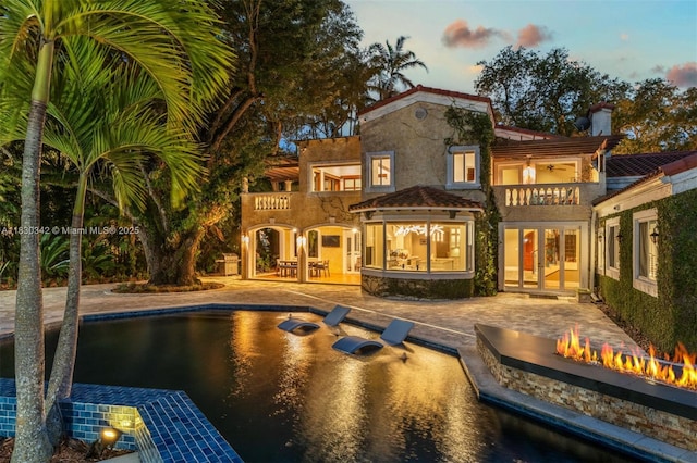 11401 SW 69th Ave, Pinecrest, FL 33156 - back of property at dusk with french doors, a balcony, stucco siding, a fire pit, and a chimney