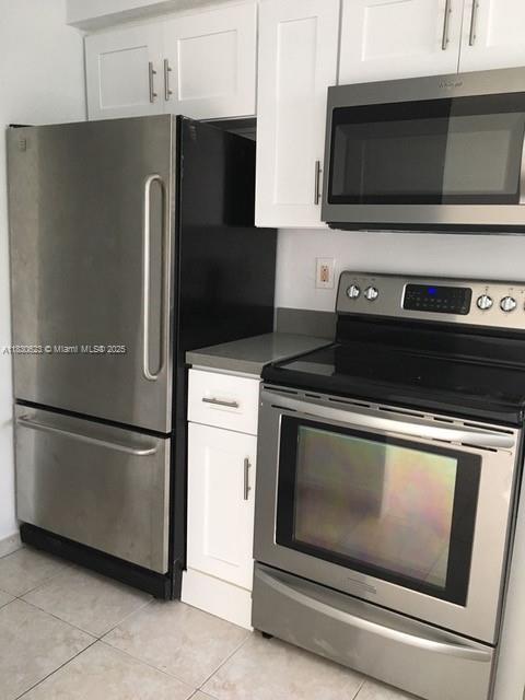 342 NW 84th Ter Unit 342, Miami, FL 33150 - kitchen featuring appliances with stainless steel finishes, white cabinetry, light tile patterned floors, and dark countertops