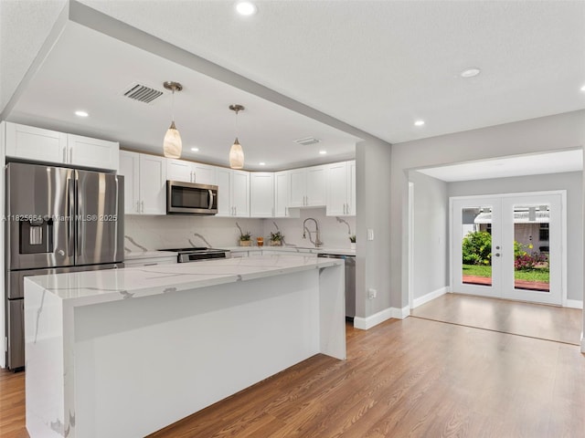 2991 NW 1st Dr, Pompano Beach, FL 33064 - kitchen with appliances with stainless steel finishes, light wood-style flooring, white cabinetry, light stone counters, and french doors