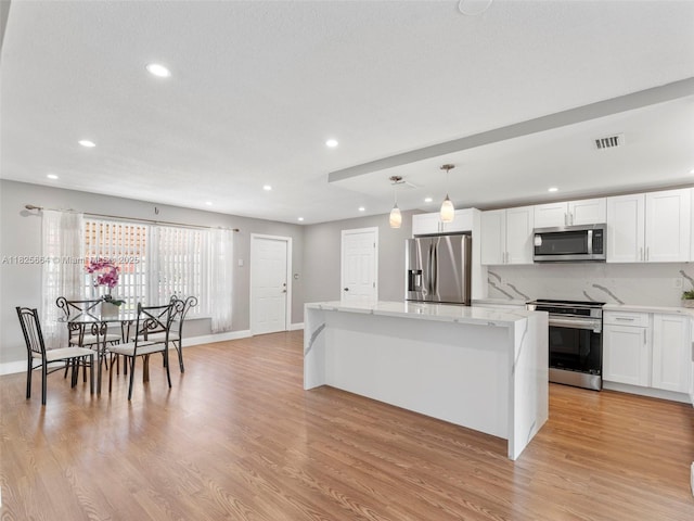 2991 NW 1st Dr, Pompano Beach, FL 33064 - kitchen with stainless steel appliances, a center island, light wood-style floors, white cabinets, and light stone countertops
