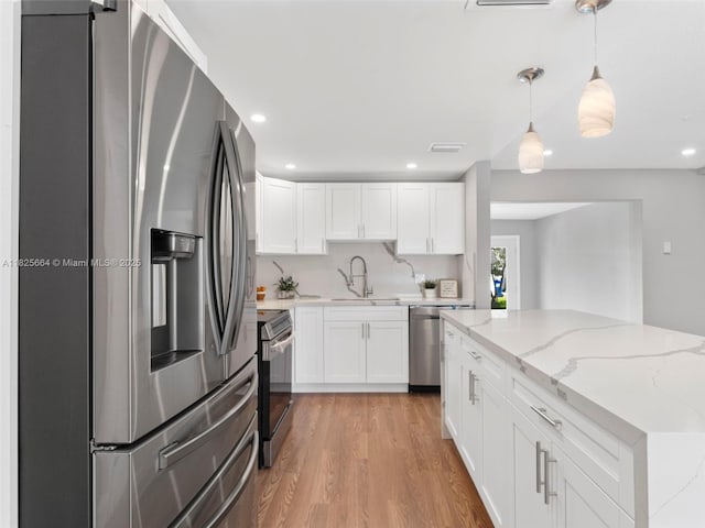 2991 NW 1st Dr, Pompano Beach, FL 33064 - kitchen featuring stainless steel appliances, white cabinets, light wood-type flooring, light stone counters, and pendant lighting