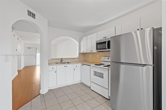 945 NE 34th Ave Unit 103, Homestead, FL 33033 - kitchen with stainless steel appliances, light countertops, white cabinetry, arched walkways, and light tile patterned floors