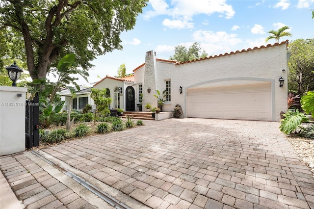 1320 Obispo Ave, Coral Gables, FL 33134 - mediterranean / spanish house with stucco siding, decorative driveway, a garage, a tile roof, and a chimney