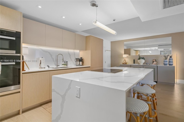 2301 Collins Ave Unit 407, Miami Beach, FL 33139 - kitchen featuring a kitchen island, a breakfast bar area, light wood finished floors, light stone countertops, and black electric stovetop