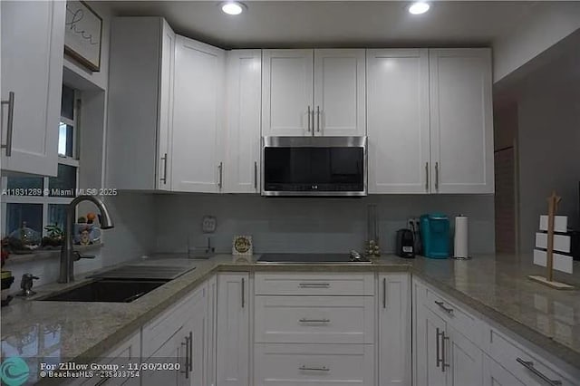 771 E 35th St, Hialeah, FL 33013 - kitchen with stainless steel microwave, black electric stovetop, white cabinets, recessed lighting, and light stone countertops