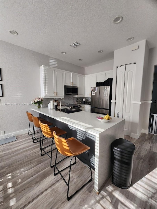 706 SW 147th Ave, Pembroke Pines, FL 33027 - kitchen featuring stainless steel appliances, a peninsula, a textured ceiling, light wood-type flooring, and a kitchen breakfast bar