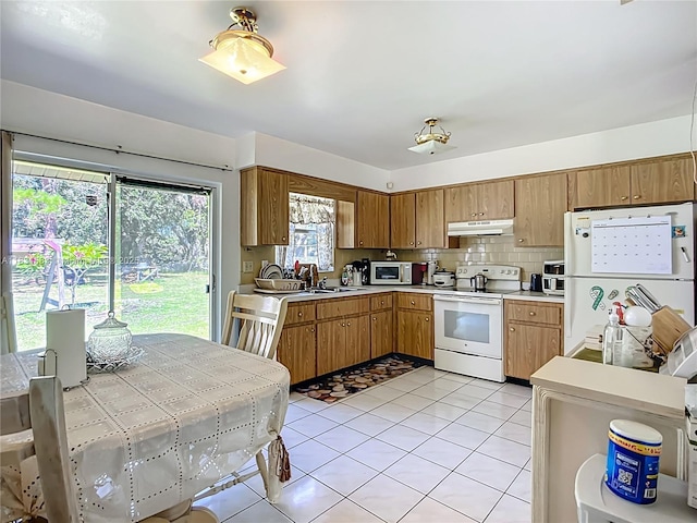 1206 E 27th St, Bradenton, FL 34208 - kitchen with white appliances, under cabinet range hood, light countertops, light tile patterned floors, and decorative backsplash
