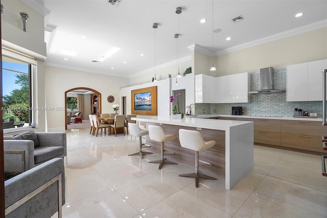 2541 Golf View Dr, Weston, FL 33327 - kitchen with wall chimney range hood, modern cabinets, arched walkways, ornamental molding, and light countertops
