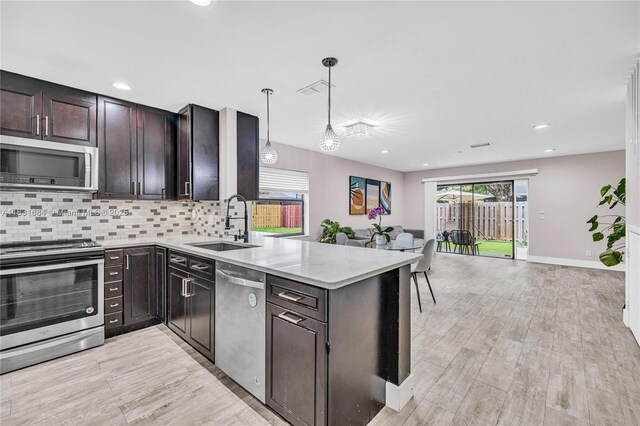 10527 NW 6th St, Pembroke Pines, FL 33026 - kitchen with appliances with stainless steel finishes, light wood-type flooring, a peninsula, decorative backsplash, and pendant lighting