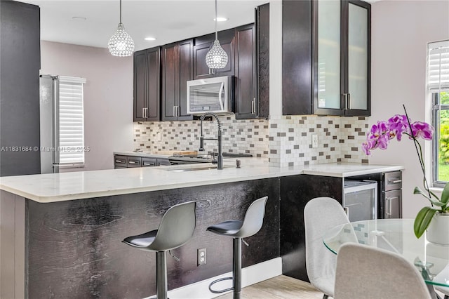 10527 NW 6th St, Pembroke Pines, FL 33026 - kitchen with stainless steel microwave, decorative backsplash, hanging light fixtures, light stone countertops, and dark brown cabinetry