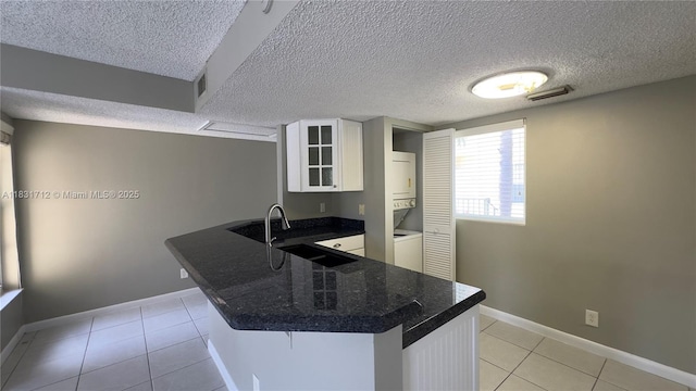 1145 Lake Shore Dr Unit 205, Lake Park, FL 33403 - kitchen featuring stacked washing machine and dryer, a peninsula, light tile patterned floors, white cabinetry, and a textured ceiling