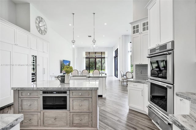 11056 Blackhawk Blvd, Davie, FL 33328 - kitchen featuring double oven, a warming drawer, light wood-style flooring, an island with sink, and white cabinets