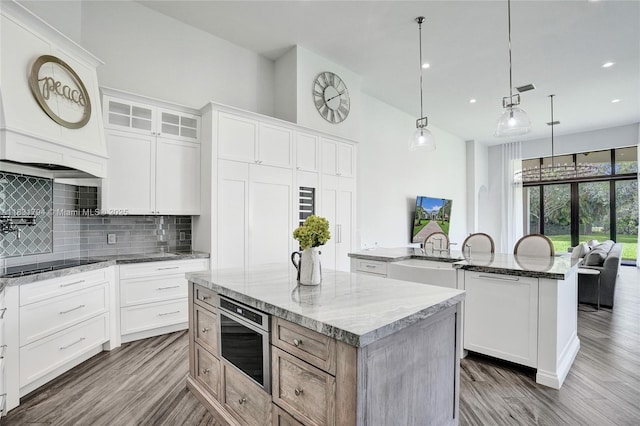 11056 Blackhawk Blvd, Davie, FL 33328 - kitchen featuring an island with sink, backsplash, black electric cooktop, wood finished floors, and recessed lighting