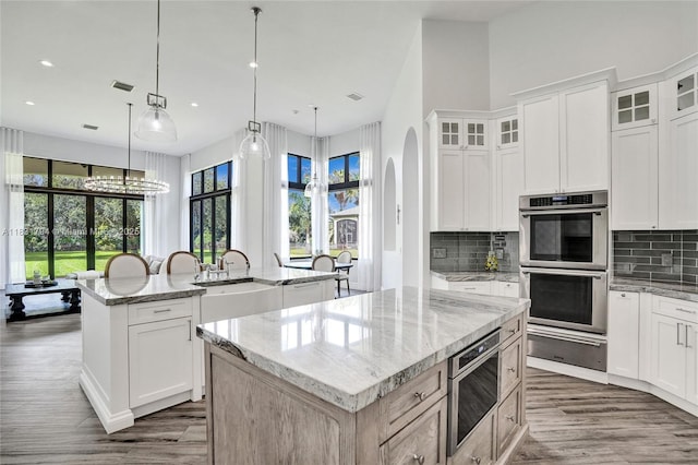 11056 Blackhawk Blvd, Davie, FL 33328 - kitchen featuring double oven, an island with sink, a warming drawer, dark wood-style floors, and decorative backsplash