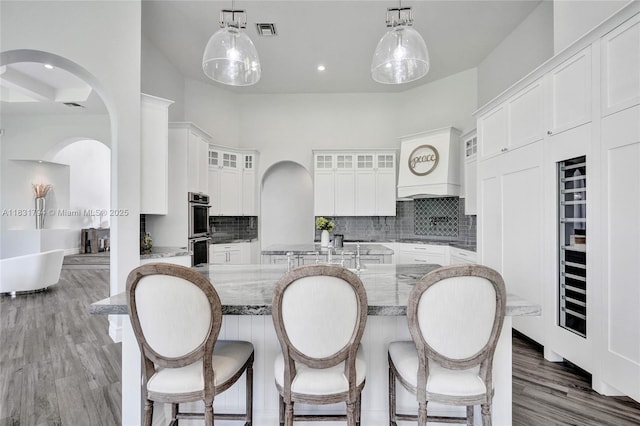 11056 Blackhawk Blvd, Davie, FL 33328 - kitchen featuring arched walkways, stainless steel double oven, glass insert cabinets, decorative backsplash, and a high ceiling