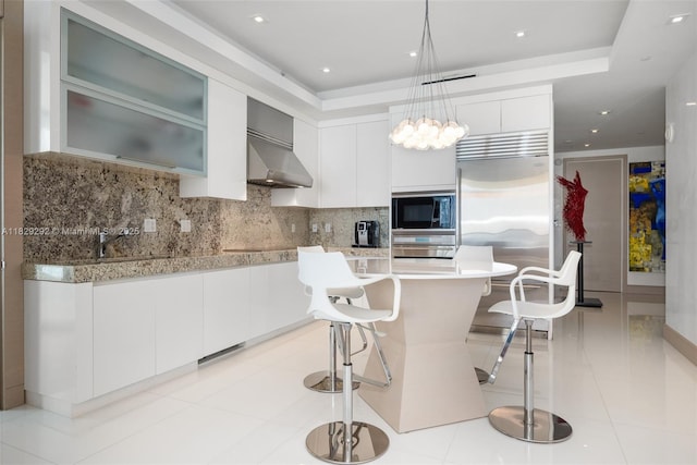 9703 Collins Ave Unit Ph-12, Bal Harbour, FL 33154 - kitchen featuring exhaust hood, built in appliances, light countertops, tasteful backsplash, and a breakfast bar area