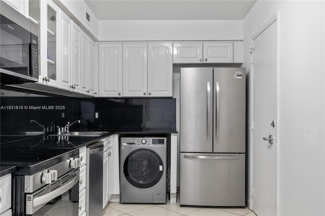 6770 Indian Creek Dr Unit 7A, Miami Beach, FL 33141 - kitchen with stainless steel appliances, washer / dryer, white cabinetry, dark countertops, and glass insert cabinets