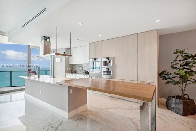 15701 Collins Ave Unit 2902, Sunny Isles Beach, FL 33160 - kitchen featuring modern cabinets, light marble finish flooring, a center island, stainless steel double oven, and tasteful backsplash