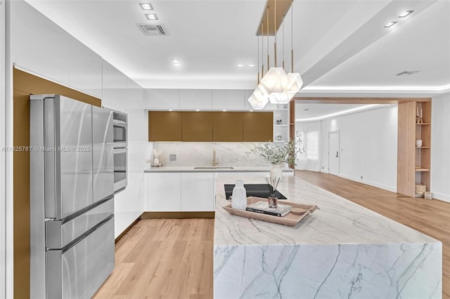 9448 Abbott Ave, Surfside, FL 33154 - kitchen with stainless steel appliances, modern cabinets, light wood-style floors, white cabinetry, and decorative backsplash
