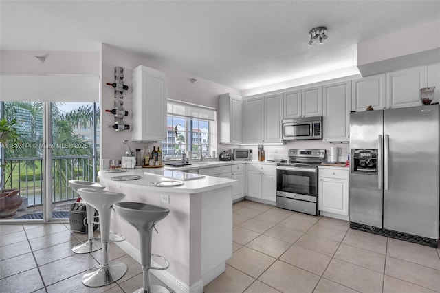 10700 NW 66th St Unit 308, Doral, FL 33178 - kitchen featuring stainless steel appliances, a peninsula, light tile patterned floors, light countertops, and white cabinets