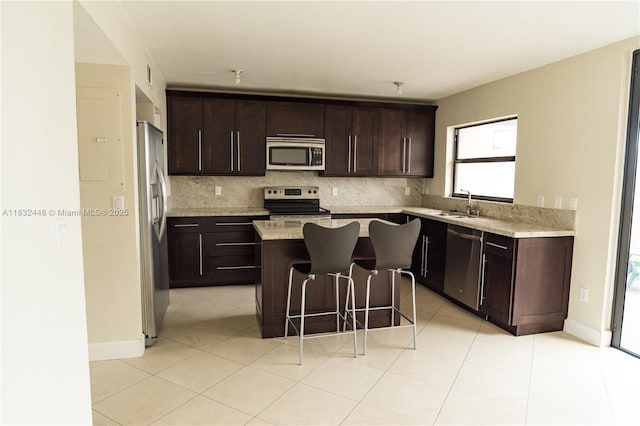 1239 NW 122nd Ter, Pembroke Pines, FL 33026 - kitchen featuring appliances with stainless steel finishes, a kitchen island, dark brown cabinetry, backsplash, and a kitchen bar