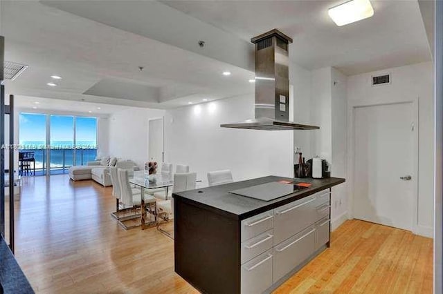 18201 Collins Ave Unit 1202, Sunny Isles Beach, FL 33160 - kitchen with island range hood, black electric cooktop, dark countertops, and light wood-type flooring