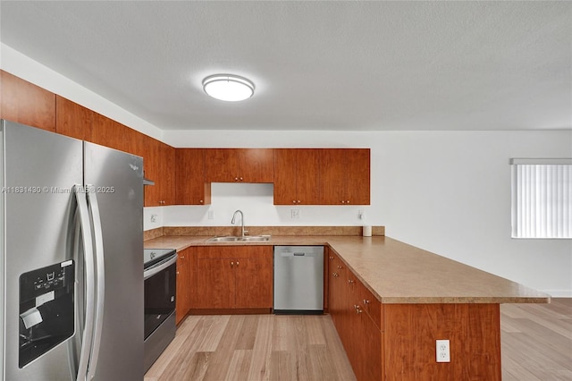 12254 SW 217th St, Miami, FL 33170 - kitchen featuring appliances with stainless steel finishes, a peninsula, light wood finished floors, brown cabinetry, and a textured ceiling