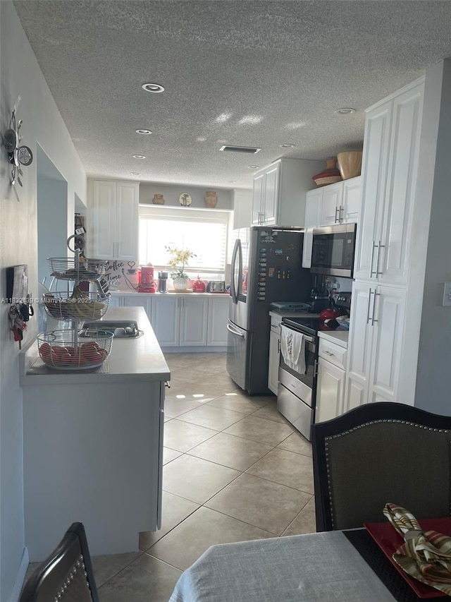 8312 NW 59th St, Tamarac, FL 33321 - kitchen with stainless steel appliances, light tile patterned flooring, white cabinetry, a textured ceiling, and light countertops
