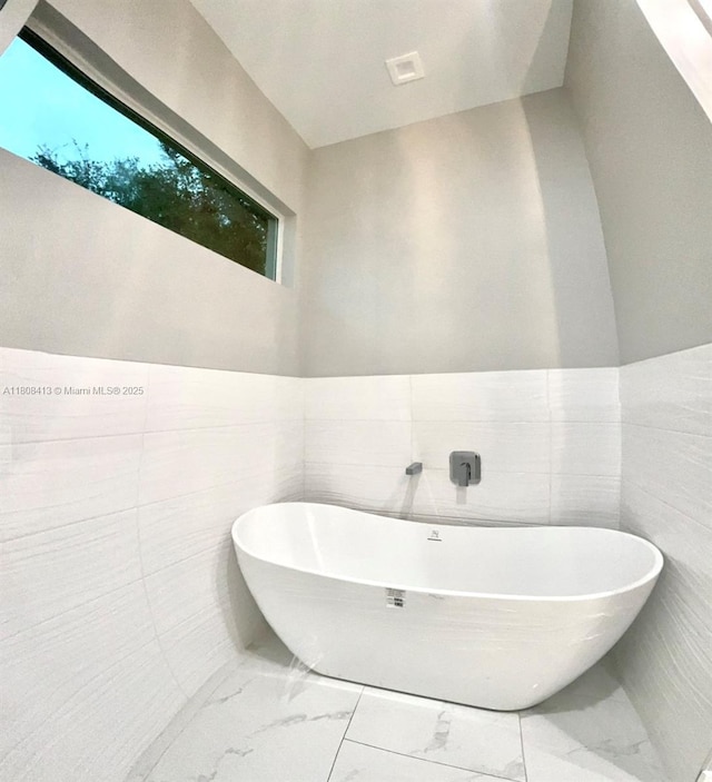 1013 SW Deauville Ave, Port St Lucie, FL 34953 - bathroom with marble look tile flooring, a freestanding tub, and tile walls