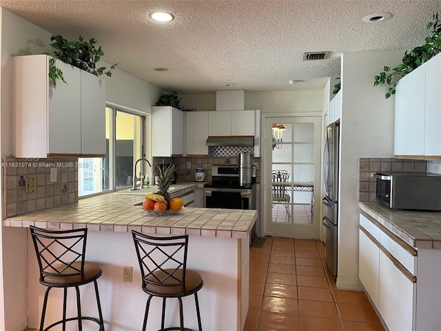 14409 SW 141st Pl, Miami, FL 33186 - kitchen featuring appliances with stainless steel finishes, a peninsula, under cabinet range hood, a textured ceiling, and backsplash