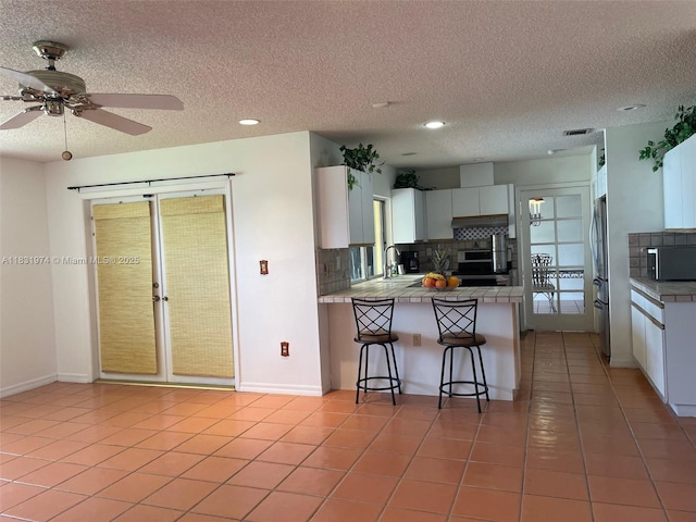 14409 SW 141st Pl, Miami, FL 33186 - kitchen featuring a peninsula, decorative backsplash, a textured ceiling, a kitchen bar, and stainless steel appliances