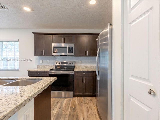 581 SW 169th Way, Weston, FL 33326 - kitchen with appliances with stainless steel finishes, light wood-style floors, dark brown cabinets, a textured ceiling, and tasteful backsplash