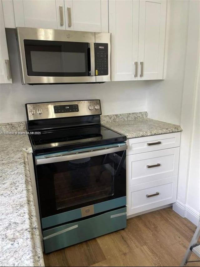791 E 22nd St, Hialeah, FL 33013 - kitchen with stainless steel appliances, white cabinetry, wood finished floors, and light stone counters
