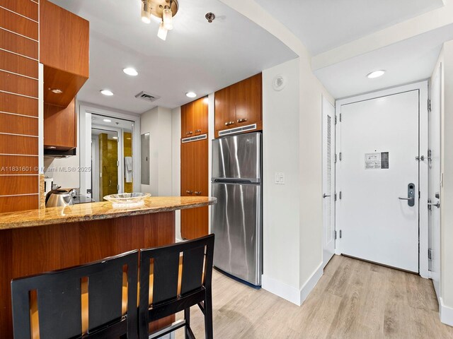 1395 Brickell Ave Unit 3310, Miami, FL 33131 - kitchen with freestanding refrigerator, light wood-type flooring, brown cabinetry, light stone counters, and recessed lighting