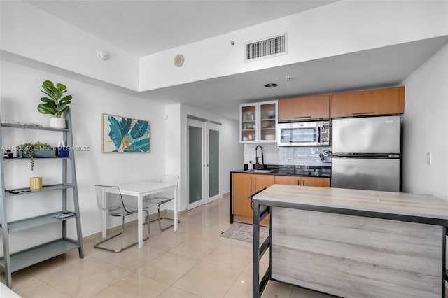 1750 N Bayshore Dr Unit 1204, Miami, FL 33132 - kitchen with appliances with stainless steel finishes, brown cabinetry, tasteful backsplash, glass insert cabinets, and light tile patterned floors